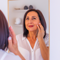 middle aged woman inspecting her skin in mirror